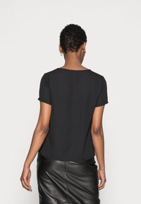 Haut noir à manches courtes avec un col rond et une texture douce, associé à une jupe en cuir noire élégante, vu de dos.