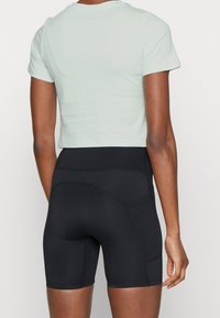 Camisa verde menta recortada combinada con pantalones cortos de ciclismo negros de cintura alta. Los pantalones cortos cuentan con bolsillos laterales y una textura suave y elástica.