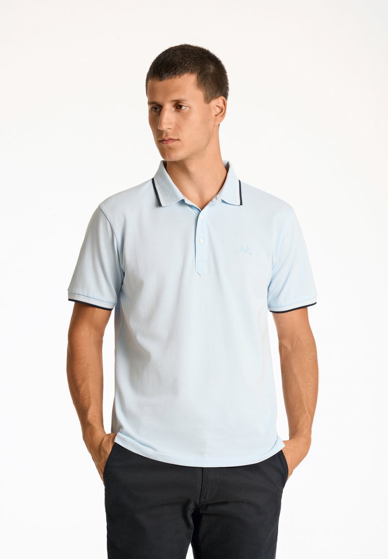 Camiseta polo azul claro con cuello, ribete en azul marino y logo bordado en el pecho. Mangas cortas y diseño de corte estándar.