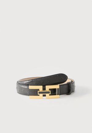 Ceinture en cuir noir avec surface texturée et boucle rectangulaire dorée entrelacée, enroulée sur un fond clair uni.