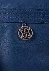 Blue leather handbag featuring a circular gold-tone hardware accent and decorative stitching along the top edge. Textured surface details visible.