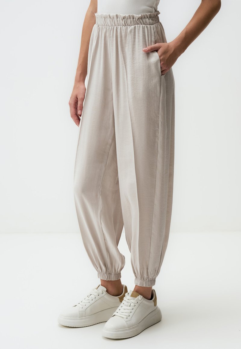 Lichtbeige, losvallende broek met een gegatherde taille en elastische manchetten, voorzien van zijzakken en een soepele textuur, gecombineerd met witte sneakers.