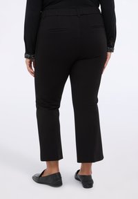 Černé kalhoty ke kotníkům s hladkým materiálem, dvěma zadními kapsami a páskem. V kombinaci s černými nazouvacími botami.