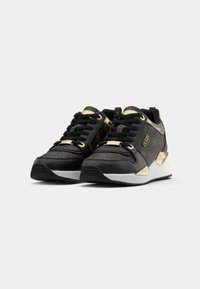 Sneaker neri e oro con tomaia a motivo, dotati di punta in pelle nera rigata, lacci piatti e suola a zeppa bianca.