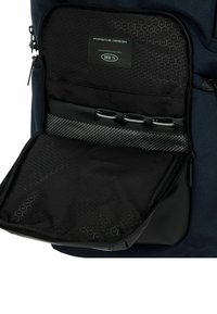 Comparto nero di uno zaino con motivo esagonale, spallacci retrattili e marchio. Tessuto testurizzato con accenti lisci.