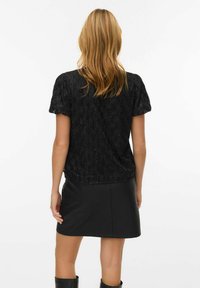 Czarny top z koralikami i krótkimi rękawami, z teksturowanym wzorem. Noszony z dopasowaną czarną skórzaną spódnicą. Smukły i nowoczesny design.