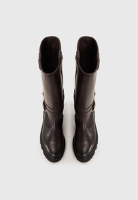 Botine din piele maro, până la genunchi, cu o textură netedă, accente aurii și o talpă groasă neagră; prezintă un design cu două curele.
