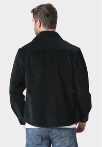 Černá kordová bunda s límcem, viditelnou texturou a knoflíky. Má mírně volný střih a rovný lem v pase.