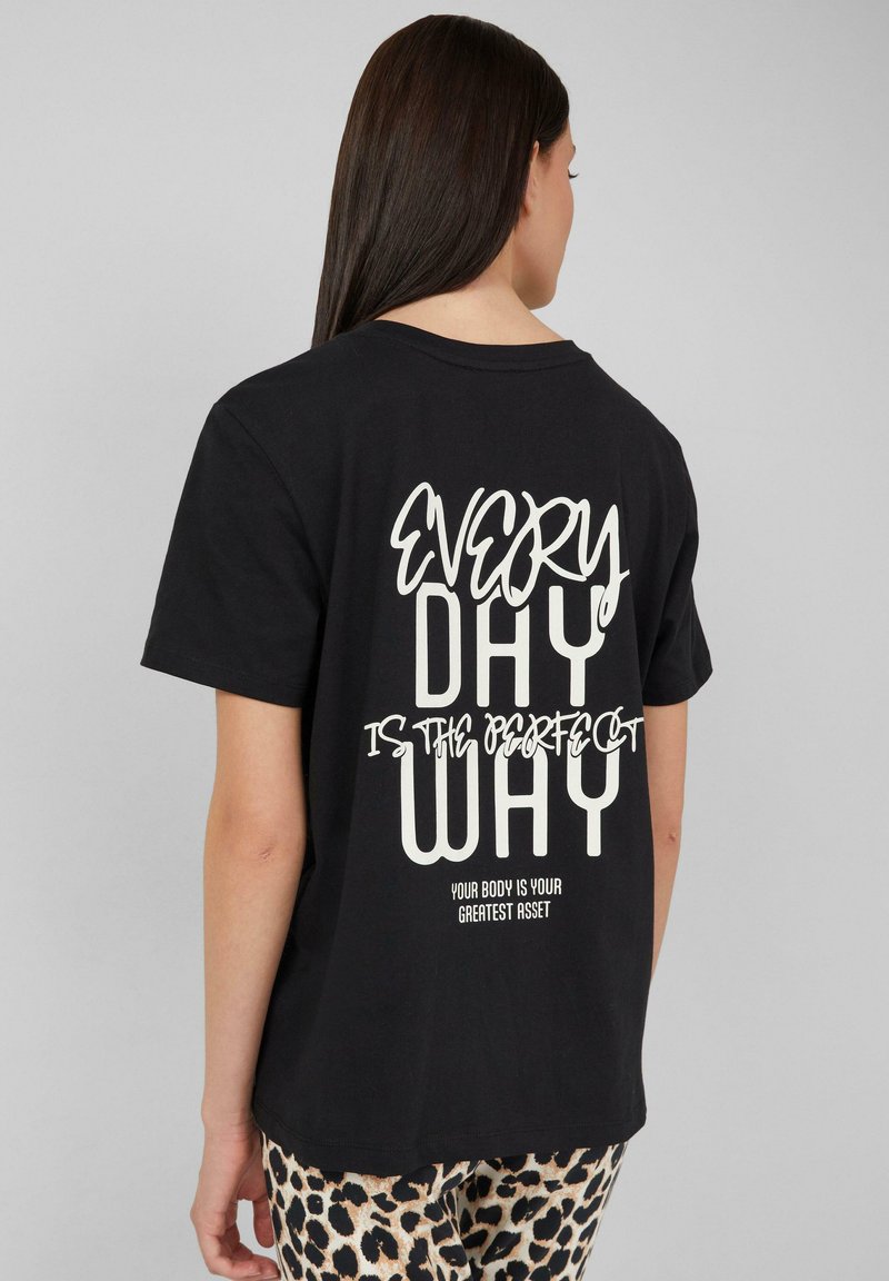 Schwarzes Baumwoll-T-Shirt mit einem auffälligen weißen Textdesign auf der Rückseite: "JEDER TAG IST DER PERFEKTE WEG" mit einem sekundären Satz darunter.