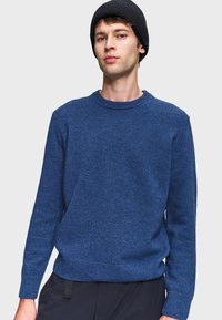 Maglione azzurro a maglia con collo rotondo, polsini e orlo a coste. Tessuto morbido con una vestibilità leggermente rilassata, abbinato a un berretto nero.
