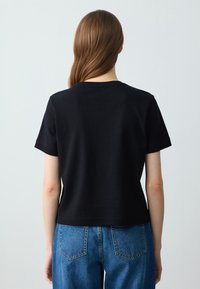 Czarny krótki t-shirt z miękkiej bawełny, z prostym okrągłym dekoltem i luźnym krojem, zestawiony z niebieskimi dżinsowymi spodniami z wysokim stanem.