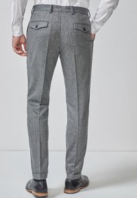 Grijze hounds-tooth broek met een getailleerde pasvorm, voorzien van twee achterzakken met knopen en een gladde textuur. G draagt met zwarte schoenen.
