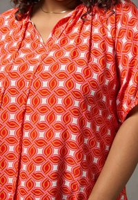 Red and white blouse featuring a geometric pattern of interlinked circles, soft material, short sleeves, and a relaxed fit.
