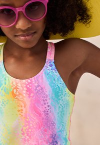 Colorful swim top featuring a gradient of pink, orange, yellow, blue, and green hues with a floral pattern; thin straps and smooth texture.