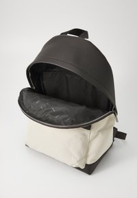 Black textured leather top with a cream canvas base, zippered opening revealing a black interior lined with repeating brand logo pattern.