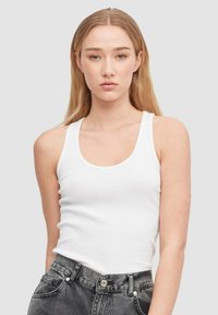 Top de tirantes anchos blanco con textura acanalada y escote redondeado, combinado con jeans de cintura alta gris oscuro. Textura suave, ajuste casual.