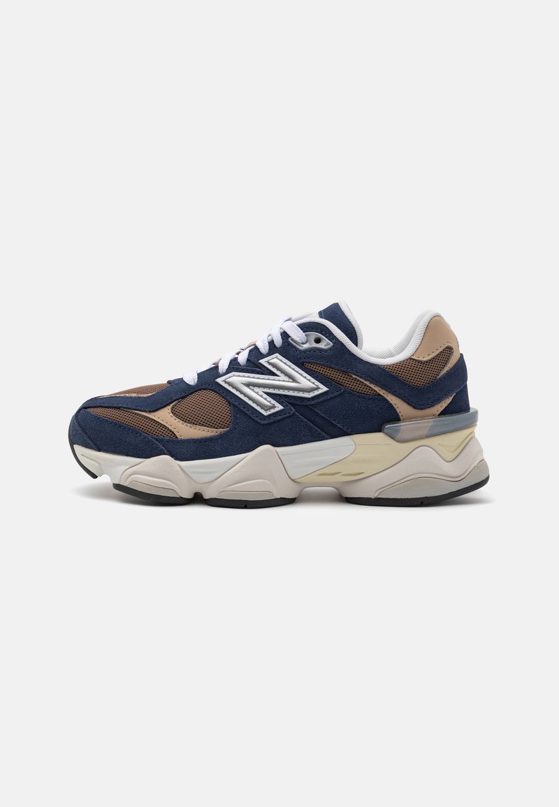 Tenisi din suede bleumarin și maro cu o talpă groasă crem, șireturi albe și accente din plasă. Prezintă un logo proeminent cu "N" pe lateral.