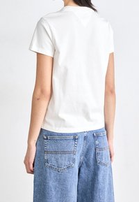 Vit bomullströja med korta ärmar, med en rundad halsringning och rak passform, ihop med blå denimjeans med vida ben.