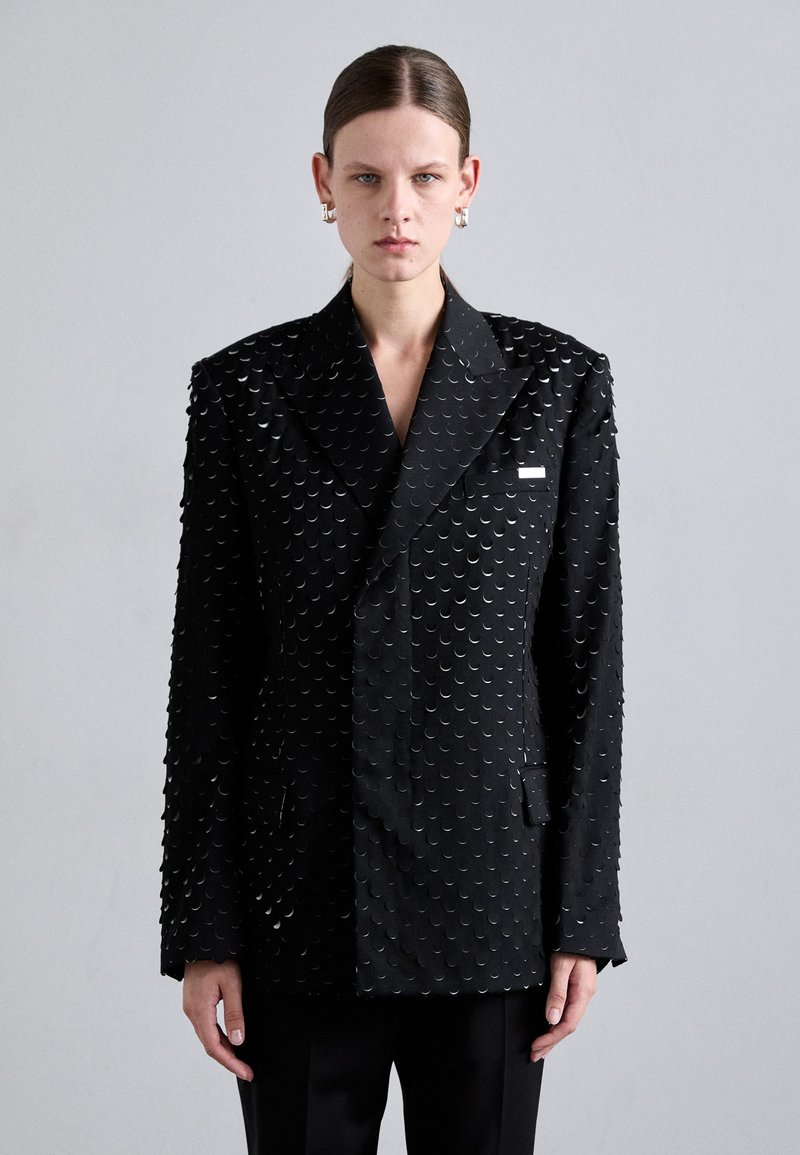 Black double-breasted blazer featuring a textured surface with circular accents, wide lapels, and front pockets. Smooth fabric with structured design.