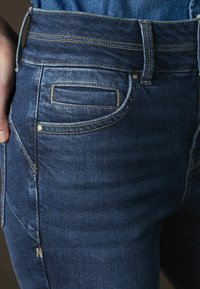 Mörkblå denimjeans med hög midja, fem fickor, kontrasterande sömmar och en subtilt urtvättad textur på tyget.
