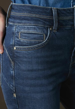 Tmavě modré džínové kalhoty se zvýšeným pasem, pěti kapsami, kontrastním prošitím a jemně vybledlou texturou látky.