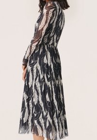 Un vestito midi a maniche lunghe con un motivo a foglie blu navy e bianche, caratterizzato da una vita stretta e un tessuto fluido e trasparente.