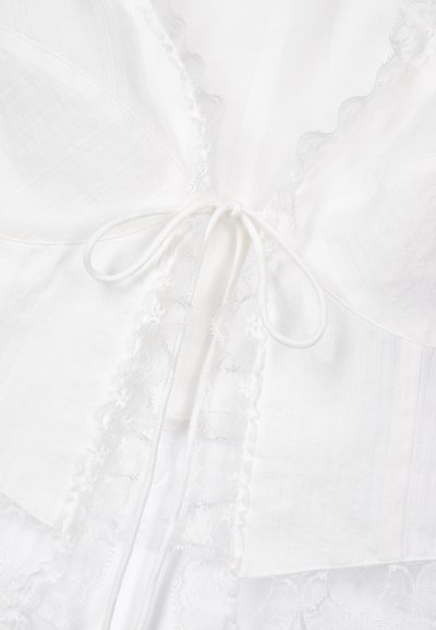 White fabric with lace trim and textured panels, featuring a drawstring closure at the neckline for adjustable fit and styling.
