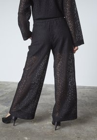 Sorte vide benbukser lavet af blonder med indviklede udskæringsmønstre, med en elastisk talje og elegante hæle.