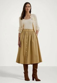 Krēmlikā sieviešu džemperis ar adījuma kabeli, beigā kurpe ar pogām un krokām, kā arī brūnas ceļgalu augstās zābaki. Gludās tekstūras un neitrālas krāsas.