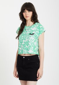 Groene en witte crop top met abstracte patronen, korte mouwen en een zwart geborduurd vleugel-detail. Gecombineerd met een zwarte denim minirok.