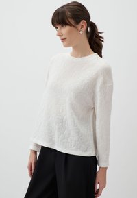 Witte gebreide trui met een bloemenpatroon, ronde halslijn, lange mouwen en een ontspannen pasvorm, gecombineerd met donkergekleurde broeken.