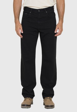 Jeans neri da uomo a gamba dritta indossati con stivali beige stringati e una camicia bianca infilata, vista frontale dalla vita ai piedi.