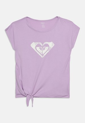 Lilafarget kortermet t-skjorte med knute foran og hvitt stilisert hjerte-logo midt på brystet.