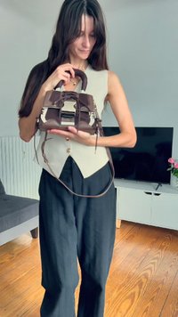 Bolso marrón y crema con un diseño estructurado, cuerpo texturizado y asas cortas, sostenido por una persona con un atuendo neutro.