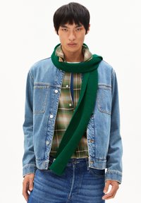 Écharpe verte côtelée enroulée autour du cou, portée avec une veste en denim par-dessus une chemise à carreaux. La combinaison présente diverses textures et couleurs.