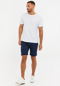 Weißes Baumwoll-T-Shirt mit rundem Ausschnitt, kombiniert mit navyblauen hochgekrempelten Shorts. Tragen mit weißen Sportschuhen, was einen lässigen Look schafft.