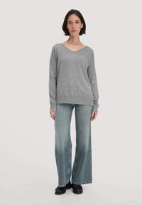 Grauer Strickpullover mit V-Ausschnitt, kombiniert mit hellblauen, weit geschnittenen Jeans. Der Pullover hat lange, lockere Ärmel und einen gerippten Saum.