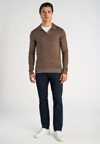 Ruskean pitkähihaisen poolopaidan rento kaulus, yhdistettynä tummansinisiin housuihin ja valkoisiin tennareihin. Ominaisuuksiin kuuluu ribbaus helmoissa ja teksturoitu neulos.