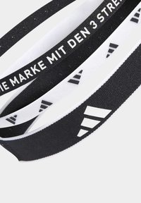 Tres bandas elásticas en blanco y negro, con rayas y logotipos, textura suave, con patrones de texto y logotipo en las superficies.