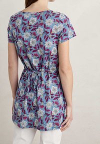 Korte mouw tuniek in blauwe stof met een bloemenpatroon in wit en bordeauxrood, voorzien van een trekkoord in de taille en een ontspannen pasvorm.