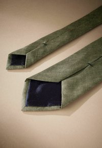 Cravate vert olive en tissu texturé avec une doublure en maille navy rectangulaire à l'extrémité, comportant deux accents cousus main.