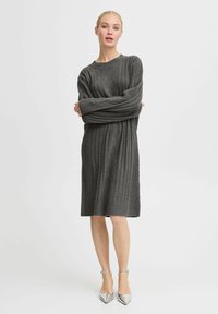 Graues gestricktes Sweatkleid mit einem strukturierten Zopfmuster, gerippten Bündchen und Saum; kombiniert mit silbernen spitzen Absatzschuhen.