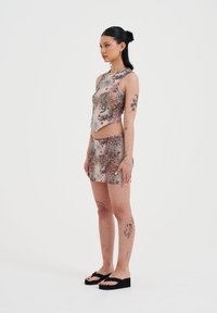 Conjunto de dos piezas que incluye una blusa corta y una falda mini, confeccionados en una tela estampada con diseños florales y de animales multicolores; sandalias planas.