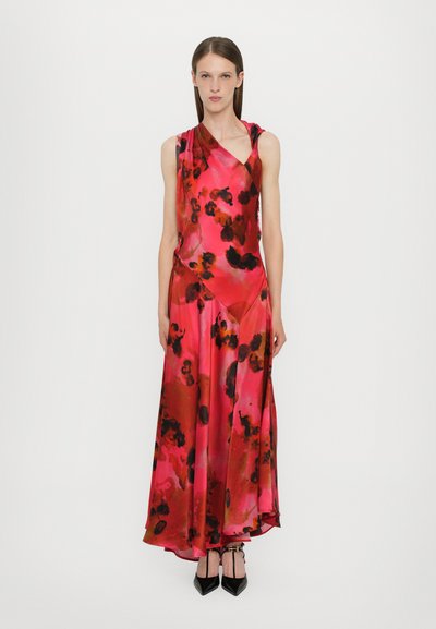 Lange, mouwloze jurk in levendig roze met een bloempatroon in diep rood en zwart. Glad, glanzend stof valt elegant tot op de grond.