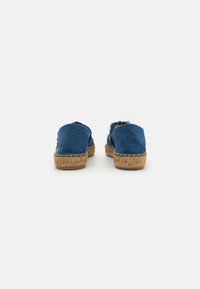 Mėlynos drobės espadrilės su pintu jūroje. Turi nusidėvėjusį kraštą ir šlepetės dizainą, demonstruojantį kasdienį ir lengvą įvaizdį.
