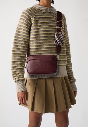 Vinrød læder crossbody taske med tekstureret overflade. Justerbar rem med et mønstret, aftageligt etui. Stribet strikket sweater og plisseret nederdel.