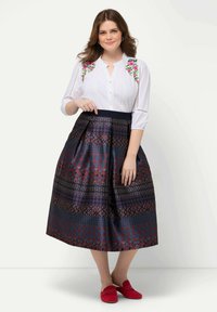 Vit blus med blommigt broderi, tillsammans med en mörk mönstrad kjol med geometriska mönster, och röda skor med detaljer.