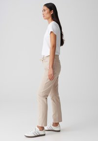 Beige katoenen broek met een trekkoord in de taille en zijzakken, gecombineerd met een witte T-shirt met korte mouwen en witte sneakers met grijze accenten.