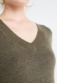 Maglione lavorato a maglia verde oliva con scollo a V, texture a costine e un sottile motivo orizzontale. Nessun hardware o decorazione visibile.