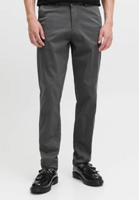 Pantalons gris en tissu lisse, avec une coupe régulière, des poches latérales et une fermeture à glissière. Associés à des chaussures noires brillantes.